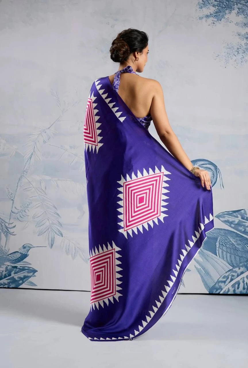 Woman wearing a purple saree with red and white patterns, standing against a light gray background.